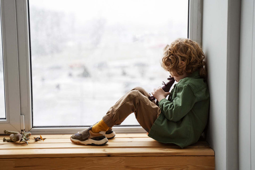sad child sitting alone by the window